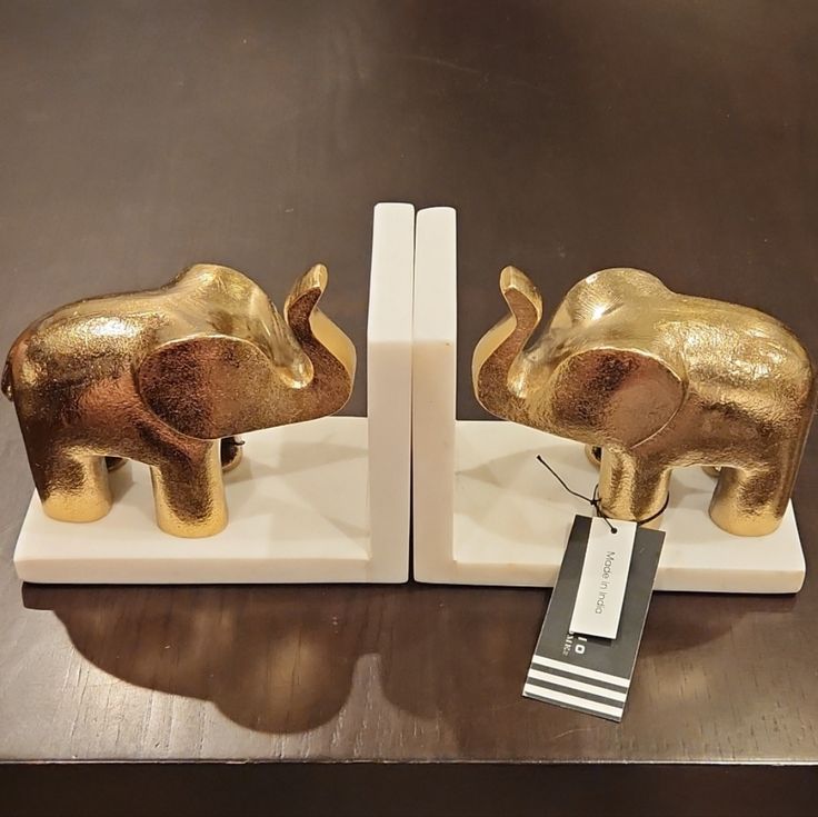 two gold elephants on white bases with a price tag hanging from the top one is for sale