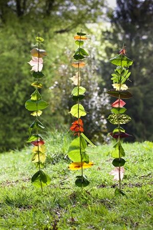 a tall metal sculpture with leaves on it's sides in the grass next to trees