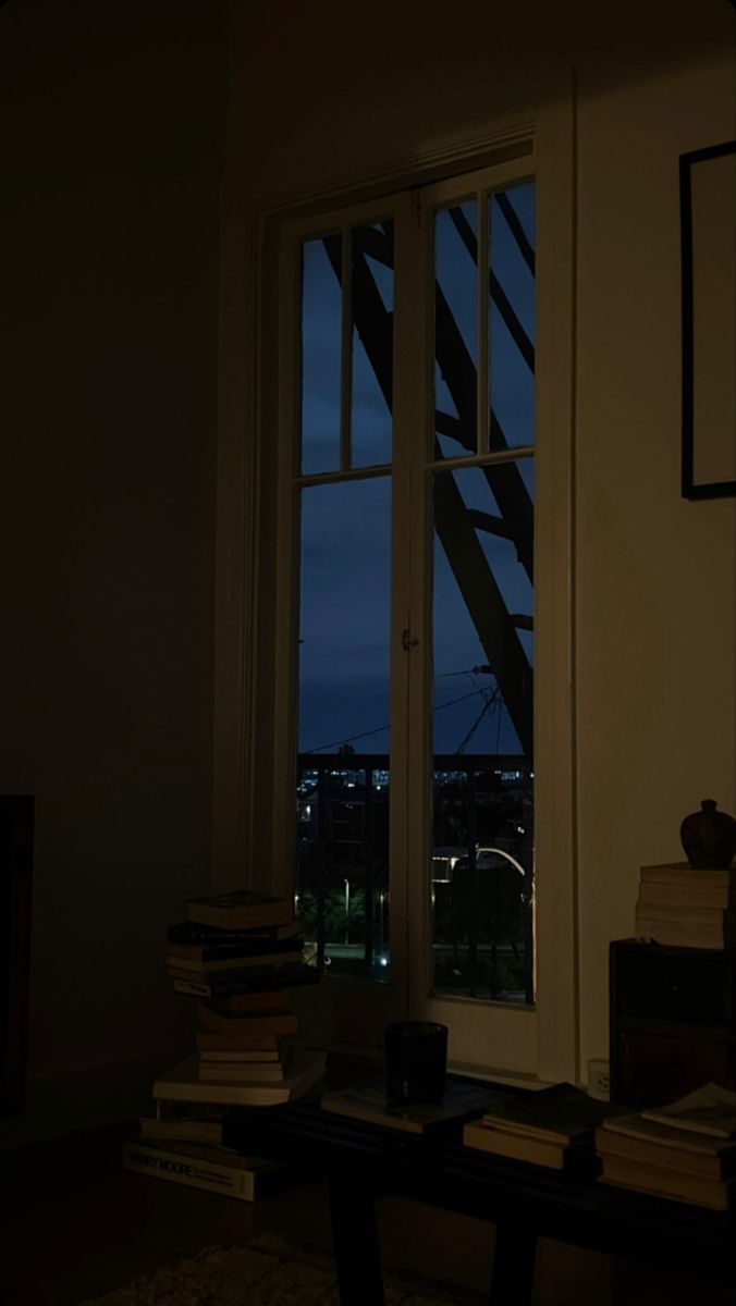 an open window in a dark room with books on the table