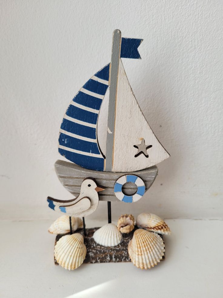 a small wooden sailboat with two seagulls and seashells on a white surface