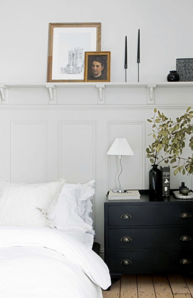 a bedroom with white bedding and black dresser next to the headboard is shown