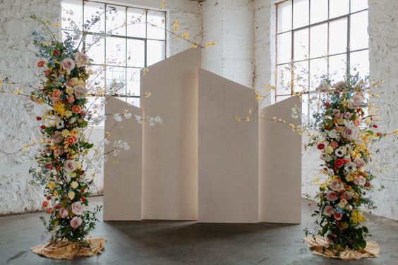 three tall vases filled with flowers on top of a floor next to two windows