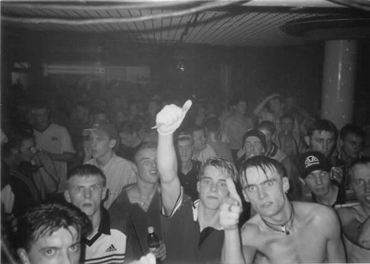 black and white photo of people at a party with one person holding up a cell phone