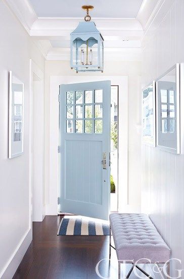 a blue front door and bench in a white hallway with wood flooring on either side