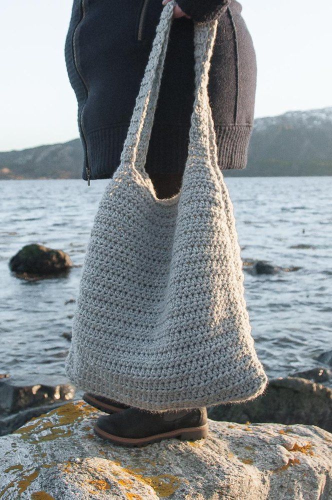 a person standing on top of a rock holding a crocheted bag in their hand