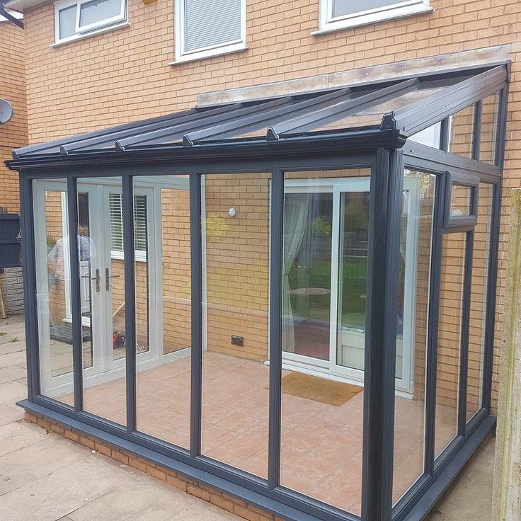 a glass enclosed patio with sliding doors on the side and brick wall behind it, in front of a house