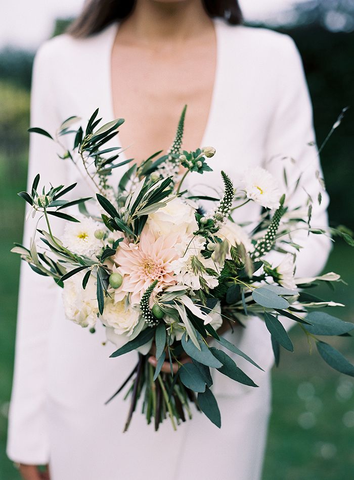 a woman holding a bouquet of flowers and greenery on her wedding day in the grass