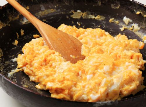 an omelet is being cooked in a skillet with a wooden spoon