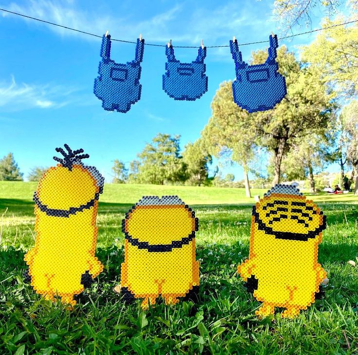 three lego minion figures are hanging on a clothes line in the grass near some trees