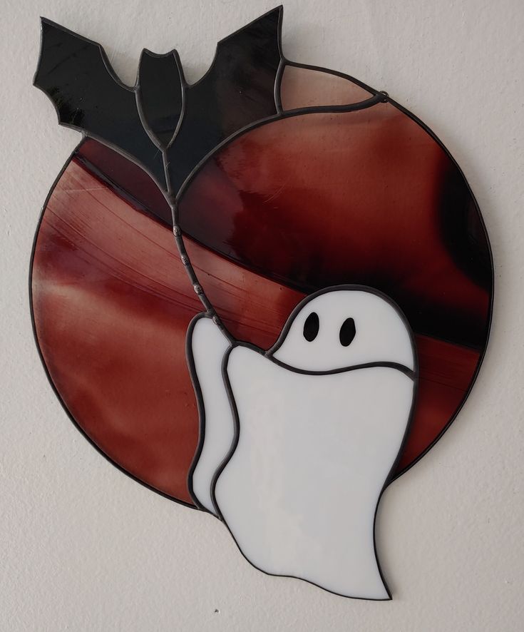 a stained glass piece with a ghost and bat on it's side, hanging from the wall