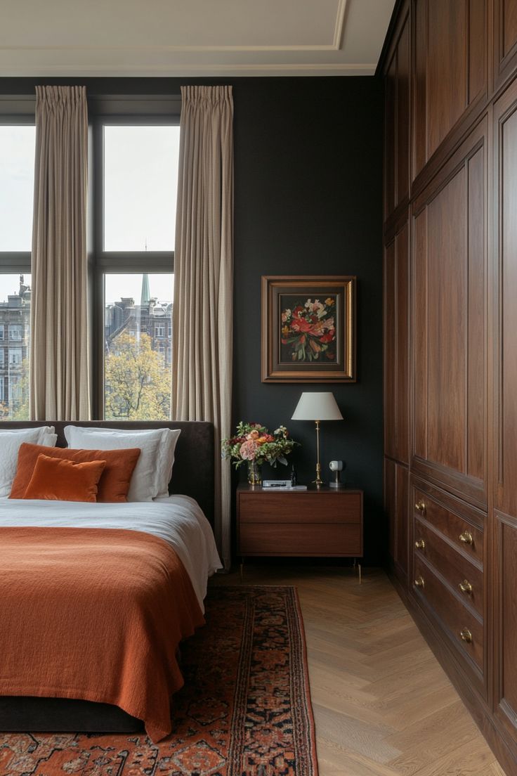 a bed in a bedroom next to two windows with drapes on them and an orange comforter