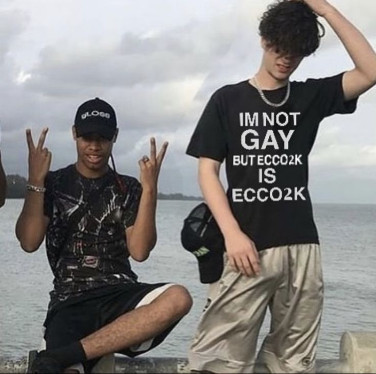 three young men sitting next to each other near the ocean with their hands in the air