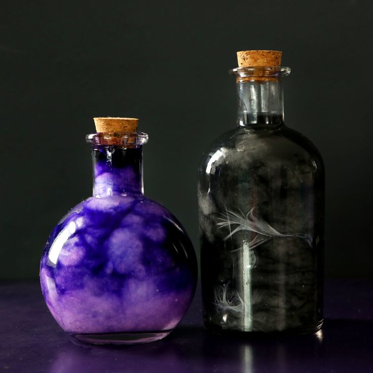 two glass bottles sitting next to each other on a purple counter top, one has a corked cap and the other is empty