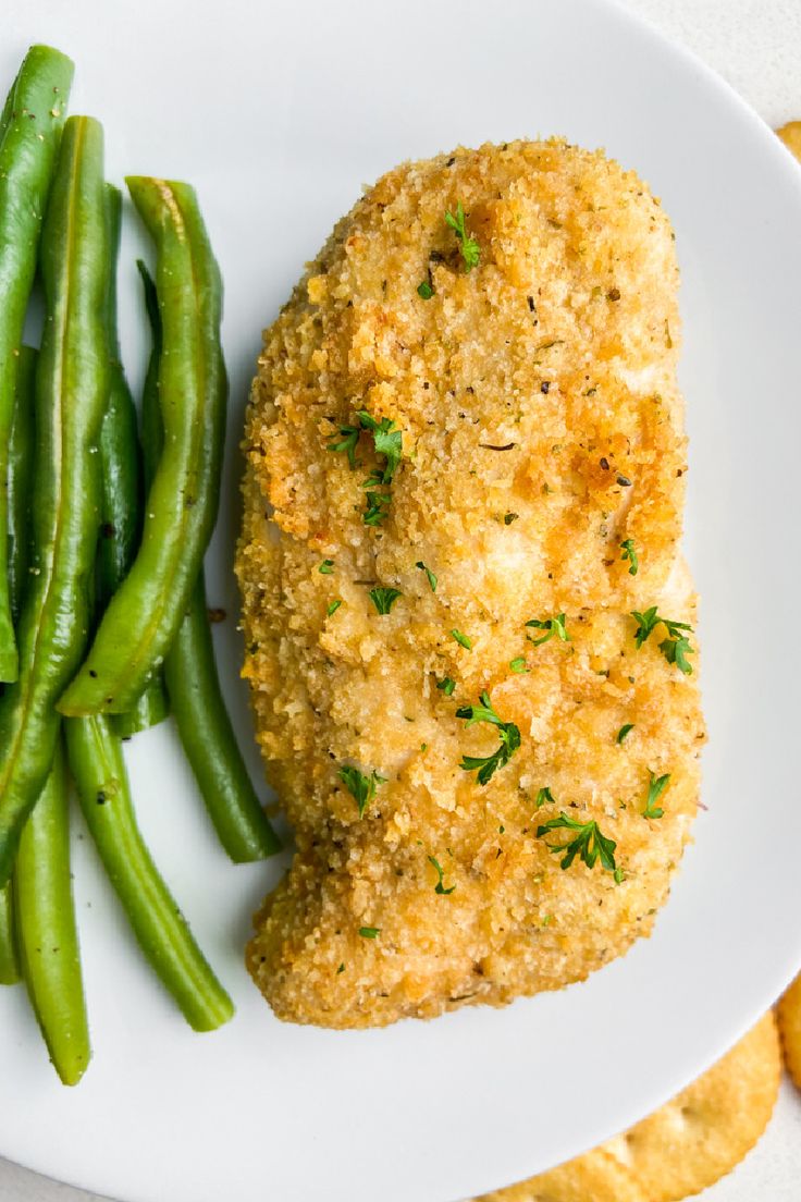 a white plate topped with chicken and green beans next to crackers on a table