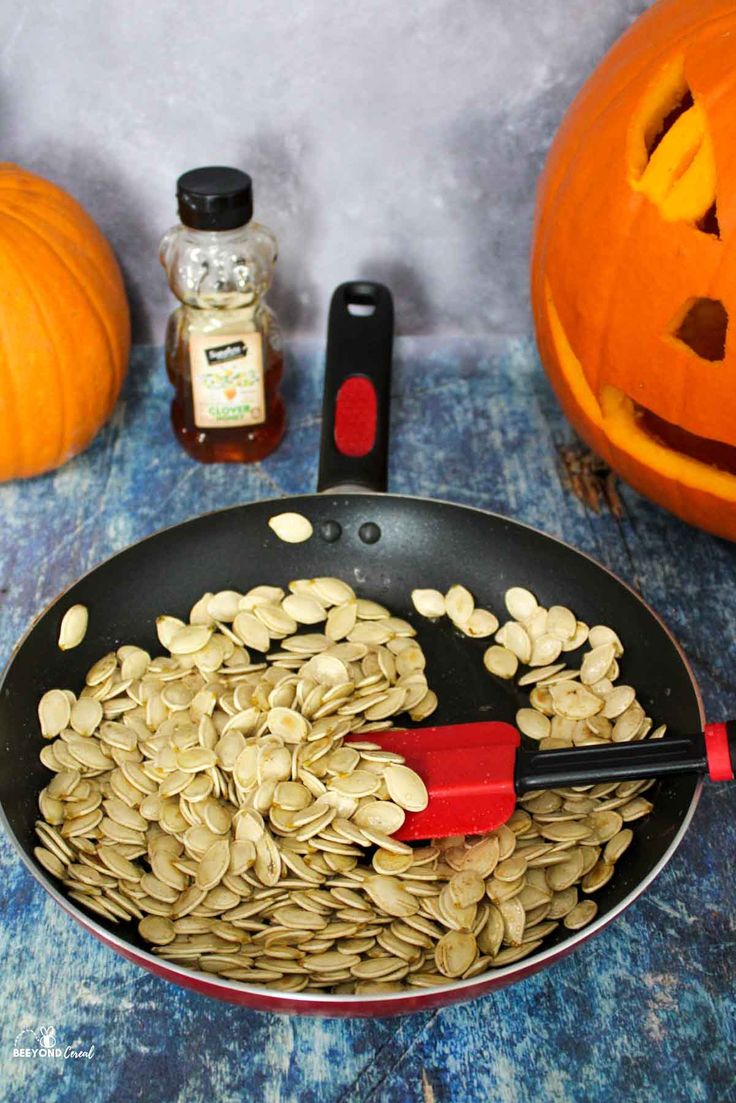 pumpkin seeds in a frying pan next to jack - o'- lanterns and spices