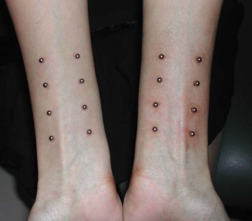 two people with matching tattoos on their arms and legs, both have small dots in them