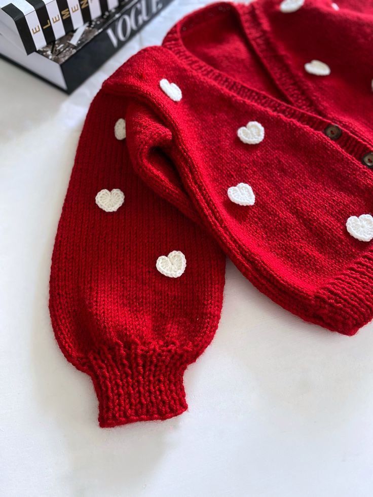 two red sweaters with white hearts on them sitting next to a black and white book