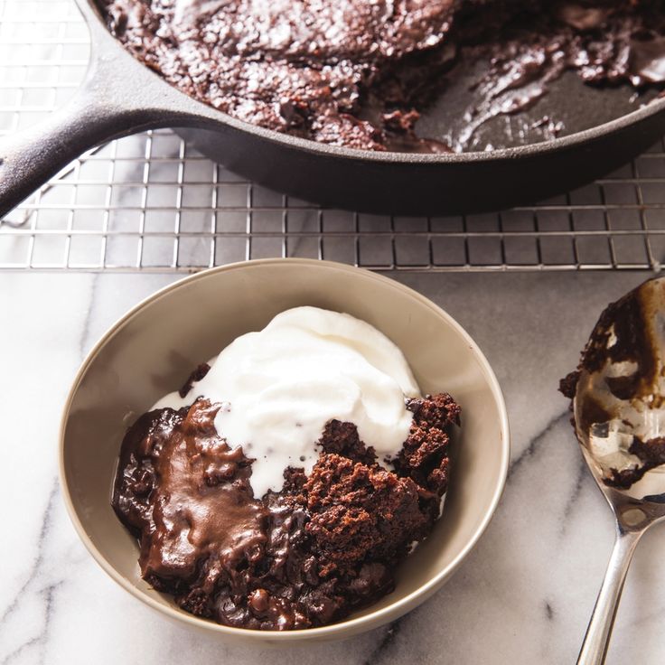 a bowl of ice cream next to a skillet filled with brownies and pudding