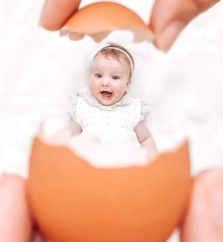 a baby is smiling while being held by someone's hands and holding an egg