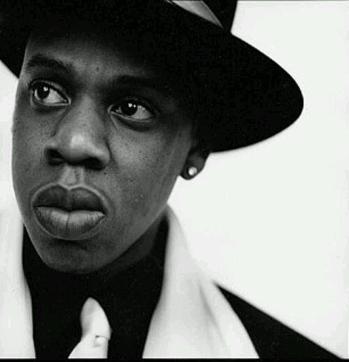 a black and white photo of a man wearing a fedora with his tongue out