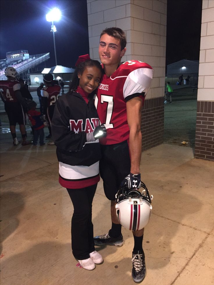 a man and woman in football uniforms posing for a photo at night with lights on