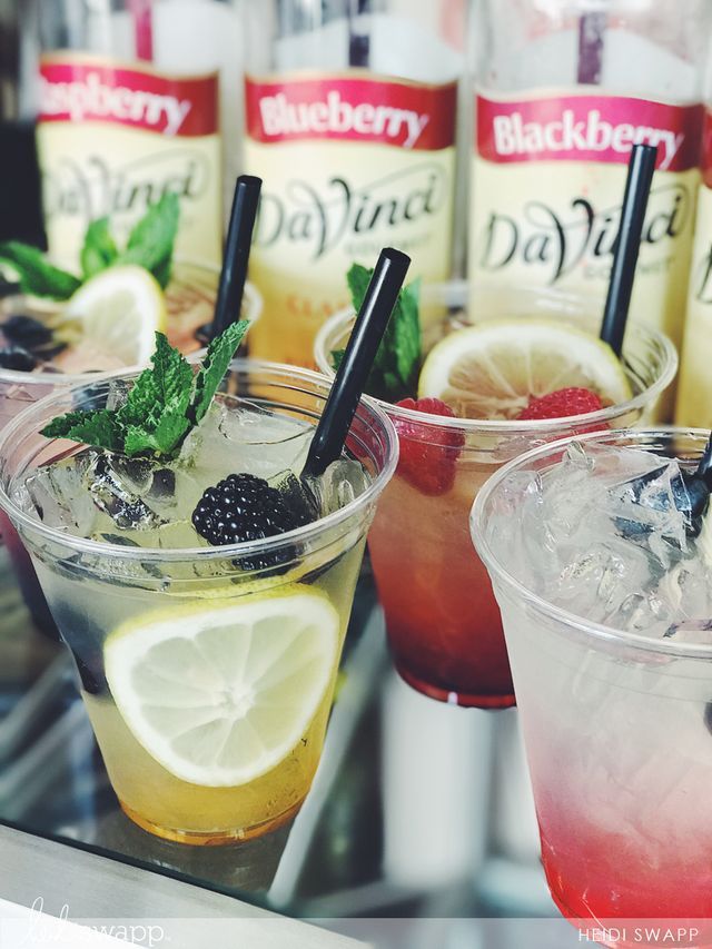 three drinks are lined up on a table with lemons and blackberries in them