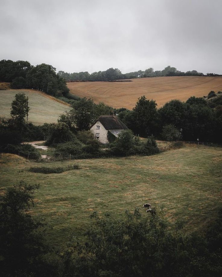 an old farm house in the middle of a field with trees and grass on both sides