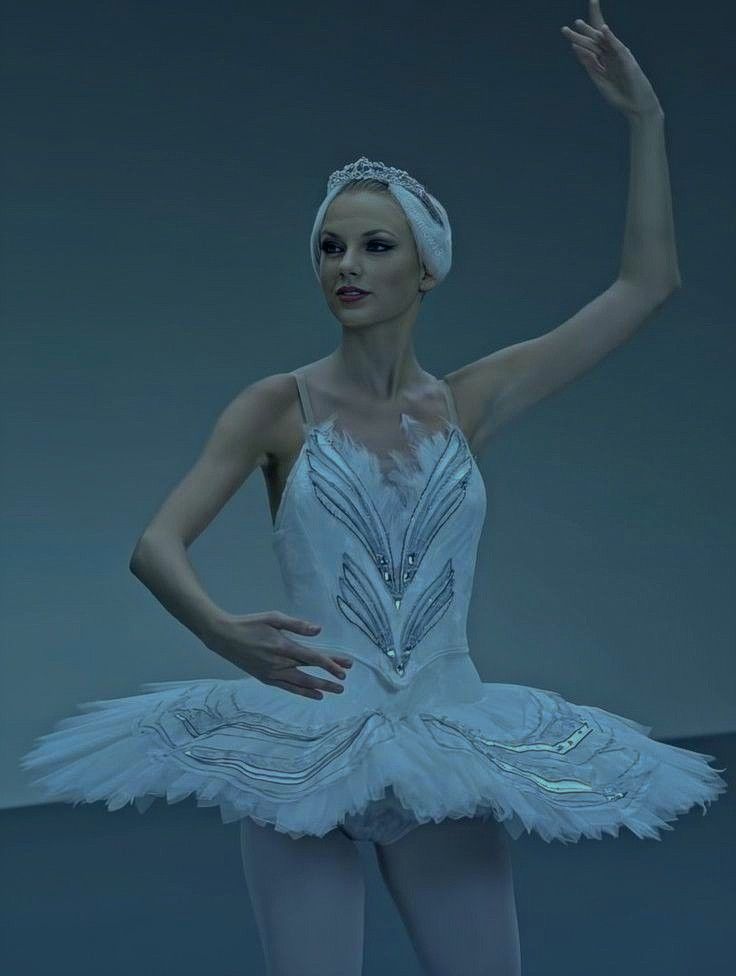 a ballerina in white tutu and headband posing for the camera with her hand up