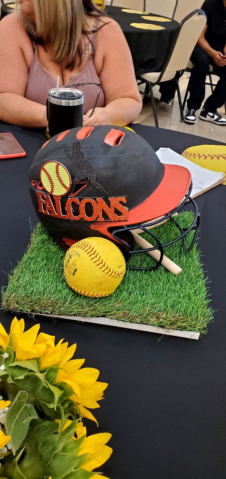 a table topped with a baseball hat and ball on top of green grass next to yellow sunflowers