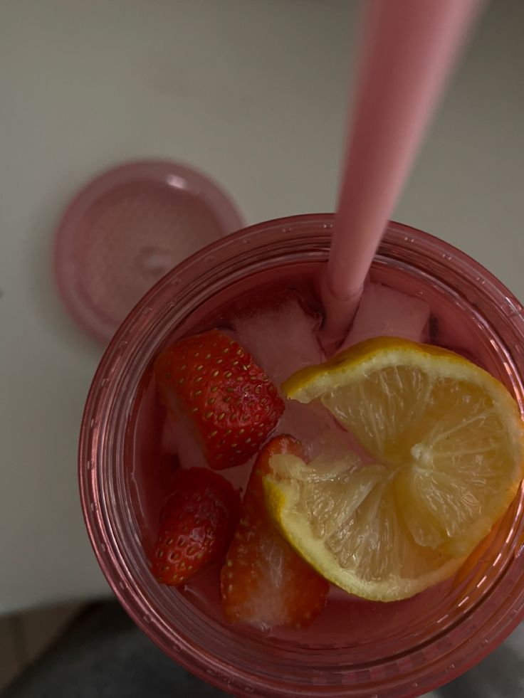 a glass filled with ice and strawberries on top of a table next to a pink cup