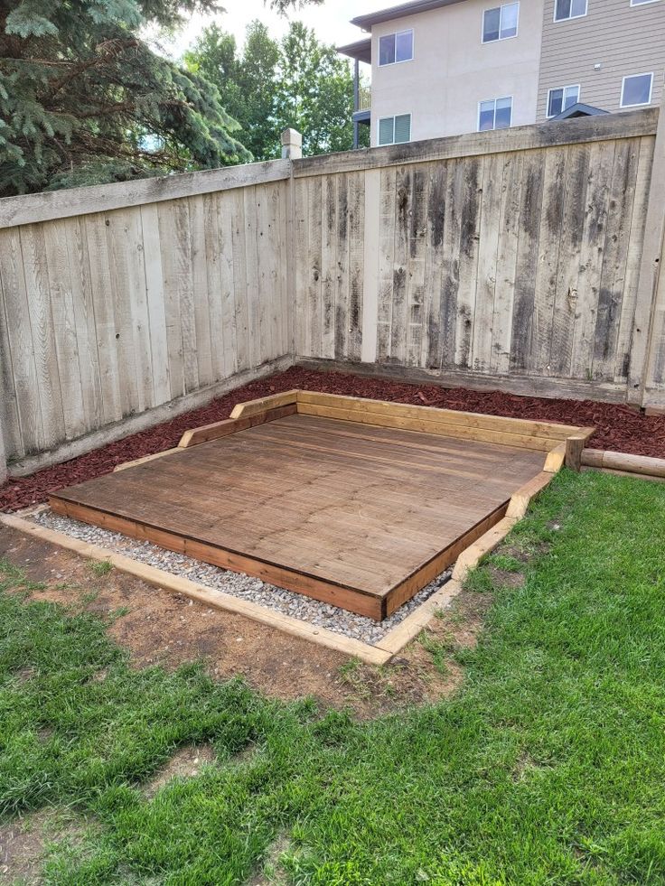 a wooden deck in the middle of a yard with grass around it and a fence behind it