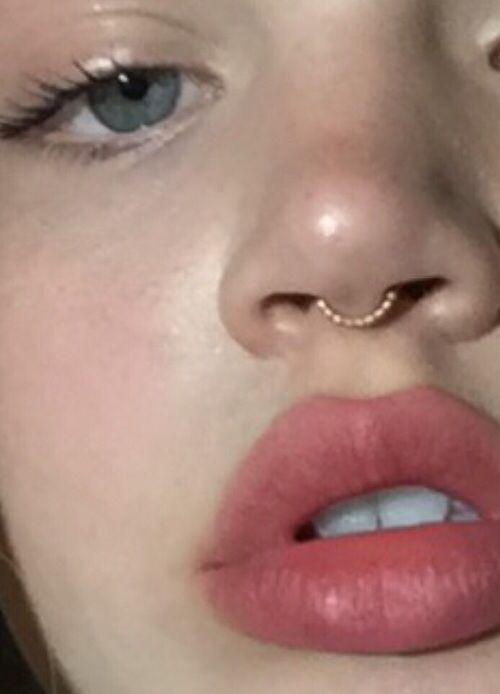 a close up of a person with a nose ring on her nose and one eye open