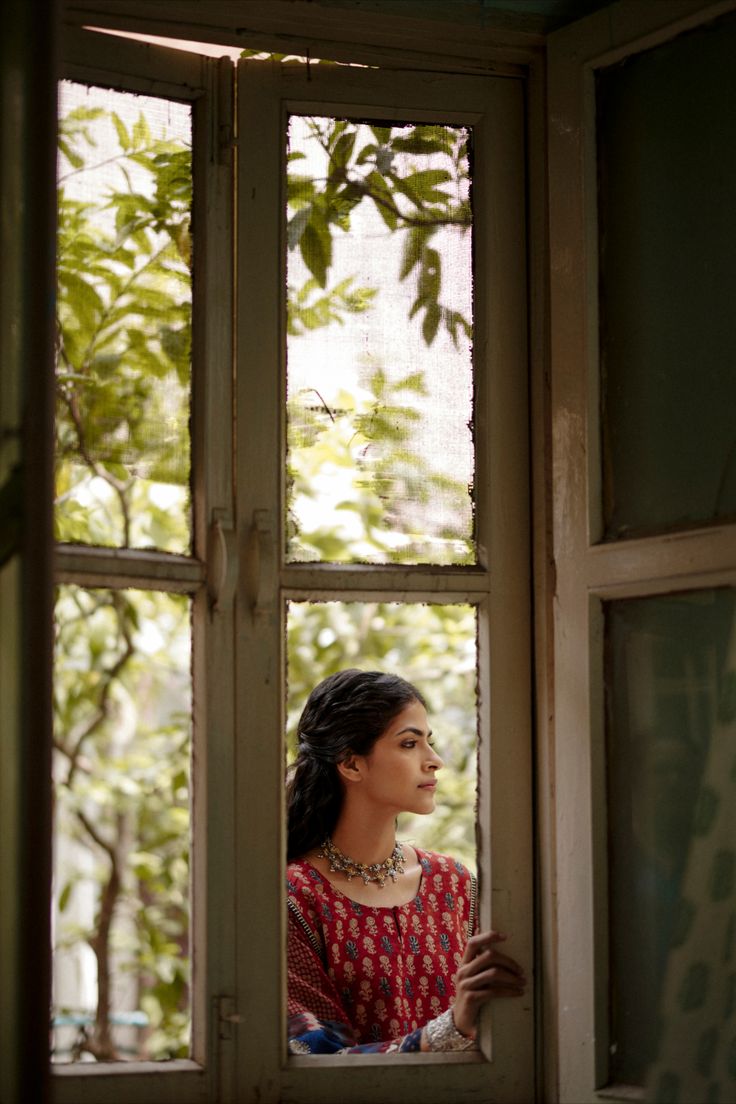 a woman standing in front of a window looking out