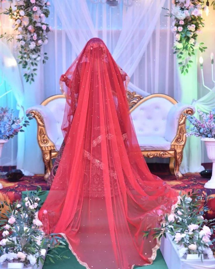 a red veil is draped over the back of a bride's dress in front of floral arrangements