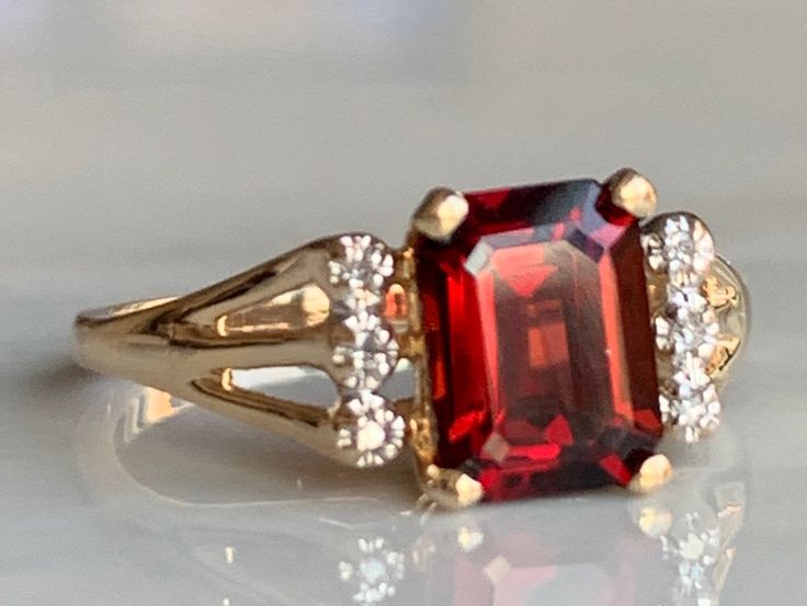 Genuine cushion emerald cut garnet ring in 14k gold. Garnet measures 8 mm x 6 mm (approximately 1.8 carats). The prongs holding the garnet stone hold 6 round cut genuine diamonds (1.3 mm each) which add to the rich claret red tones of the stone and the shank/band is made completely of 14K gold. Ring weighs 2.3 grams. Size 6.5 and can be sized +- 3.5 sizes by adding sizing to your order for 45- here: https://www.etsy.com/listing/700488426/ring-sizing-request-resizing-order Details: Ring is stampe Heirloom Emerald Cut Ruby Ring For Formal Occasions, Formal Emerald Cut Ruby Birthstone Ring, Formal Emerald Cut Ruby Ring, Classic Octagon Ruby Ring For Anniversary, Classic Radiant Cut Ruby Ring For Formal Occasions, Classic Red Emerald Cut Birthstone Ring, Formal Rectangular Garnet Rings, Garnet Ring Vintage Square, Gold Garnet Ring Vintage