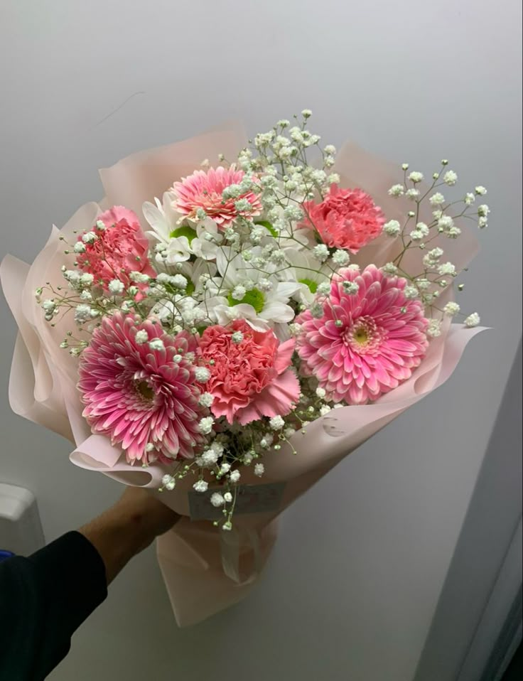 a bouquet of pink and white flowers is being held by a person's hand