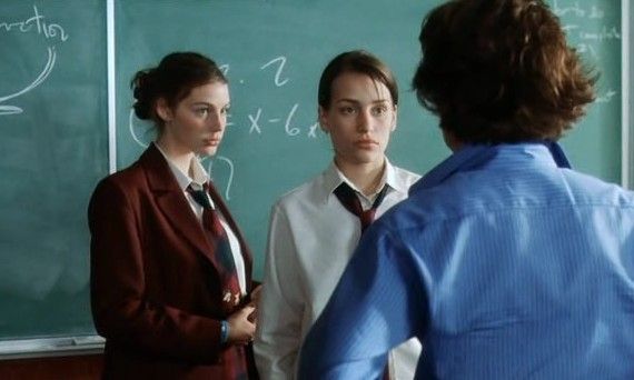 three people standing in front of a blackboard with writing on it and one person wearing a tie