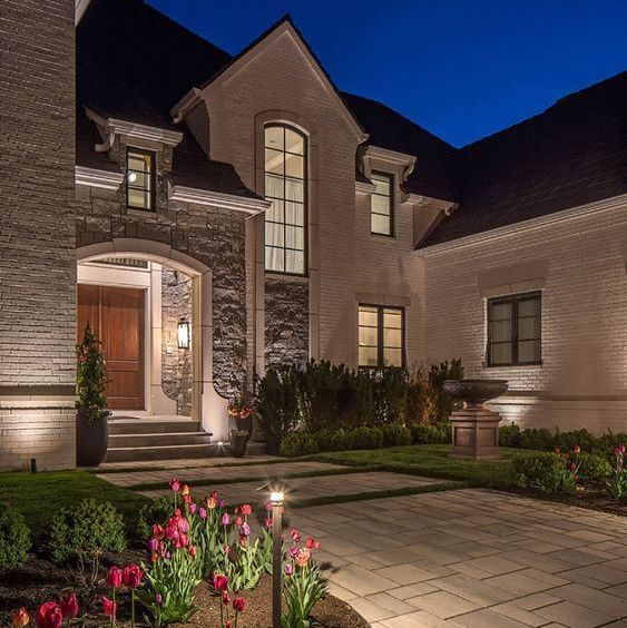 a house that is lit up at night with flowers in the front yard and landscaping around it