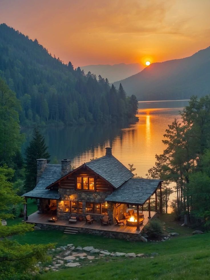 the sun is setting over a lake with a cabin on it's shore and mountains in the background