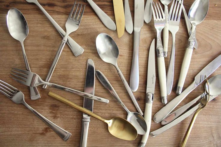 an assortment of spoons and forks laid out on a wooden table with one fork in the middle