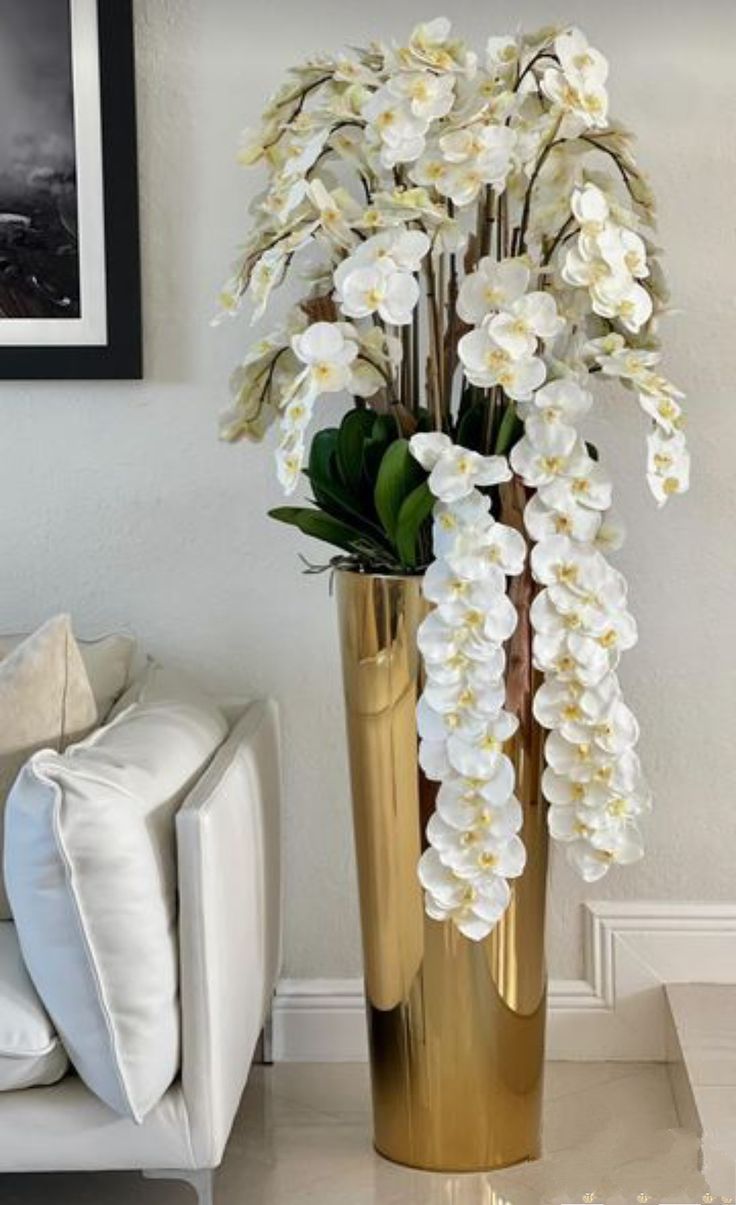 a gold vase filled with white flowers on top of a table next to a couch