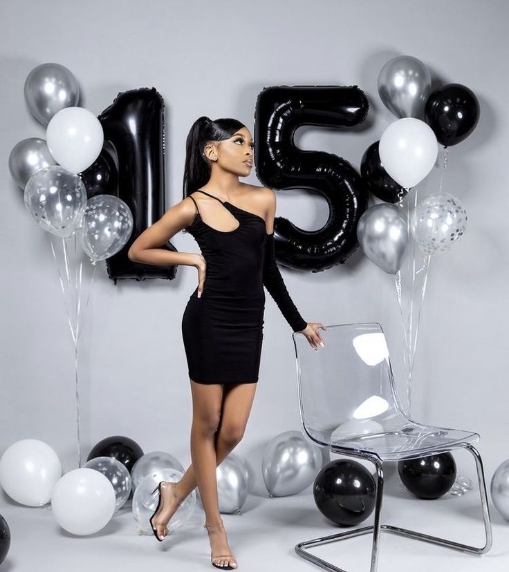 a woman in a black dress standing next to balloons and a chair with the number twenty five on it