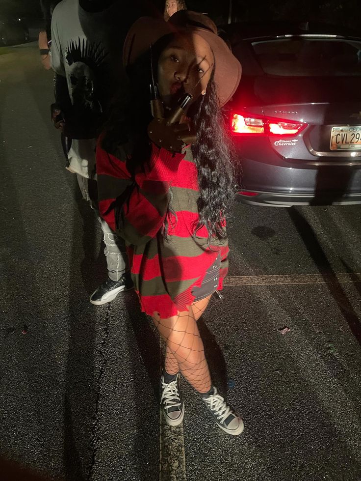 a woman in a red and black striped dress is standing on the side of the road