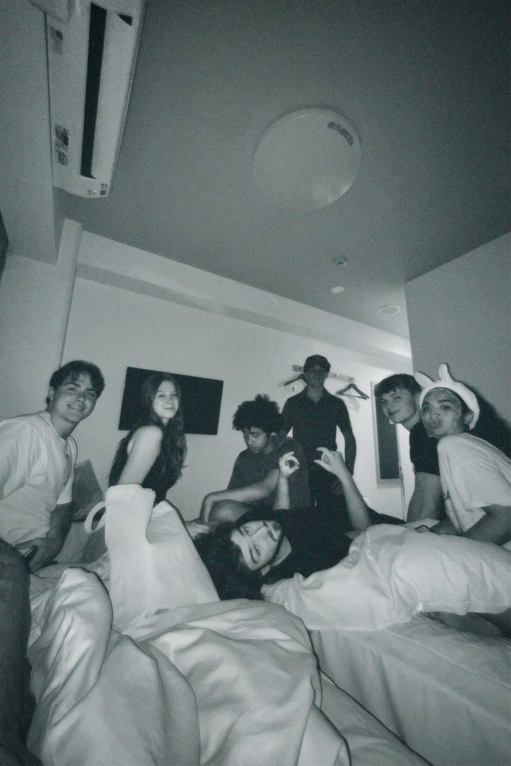 black and white photograph of four people sitting on a bed in a room with pictures above them