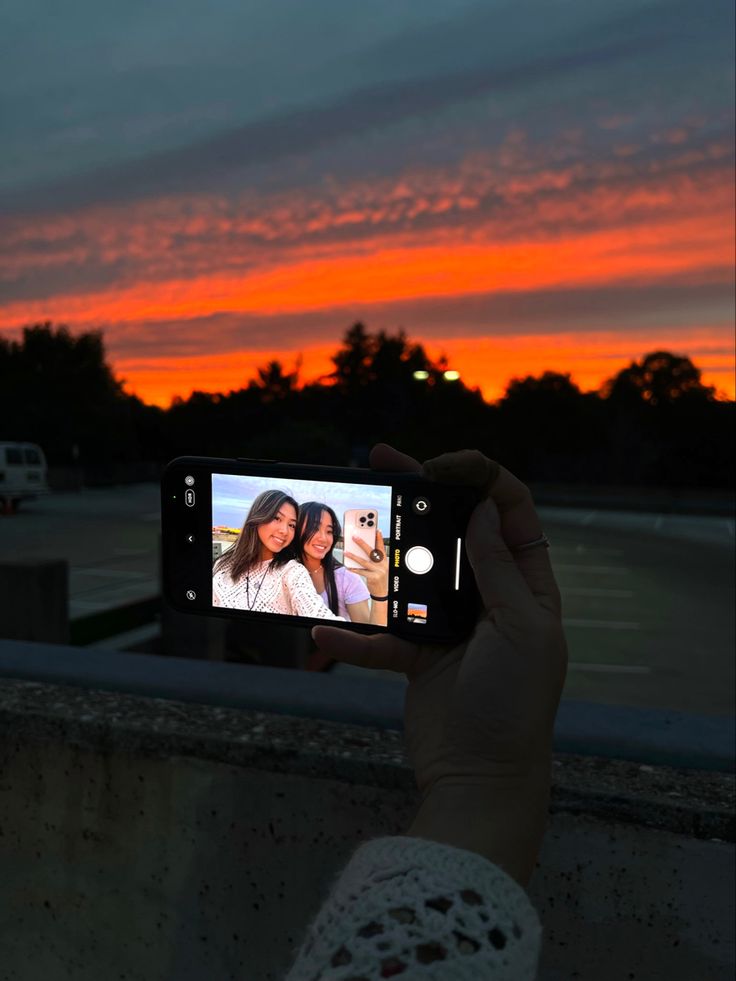 a person holding up a cell phone to take a photo with the sunset in the background