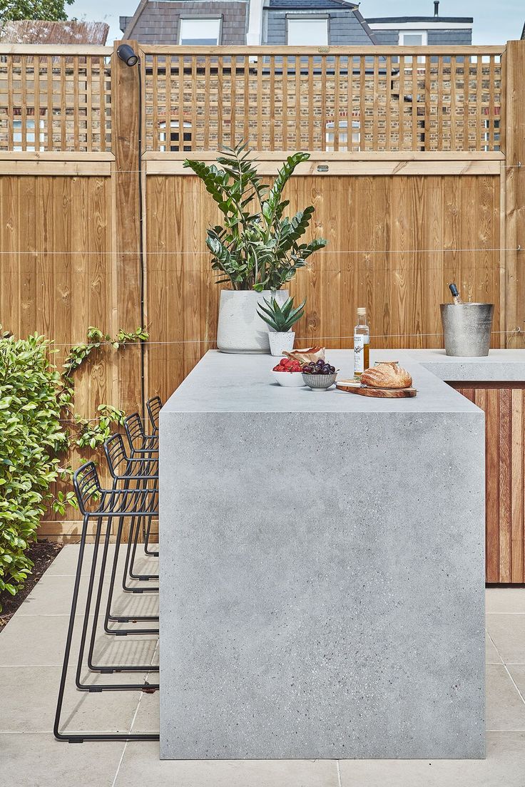 an outdoor kitchen with concrete counter tops and potted plants on the table in front of it