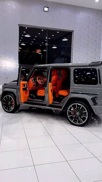 a grey and orange jeep is parked in front of a large glass building with its doors open