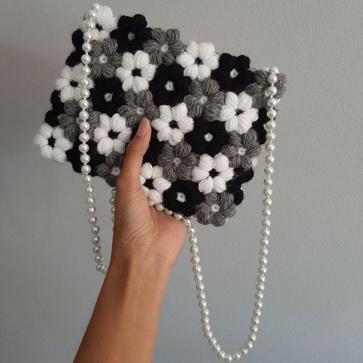 a hand holding a black and white crocheted purse with pearls on the chain