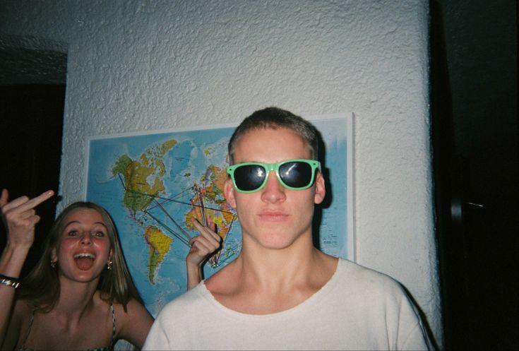 a young man wearing green sunglasses standing next to a woman in front of a map