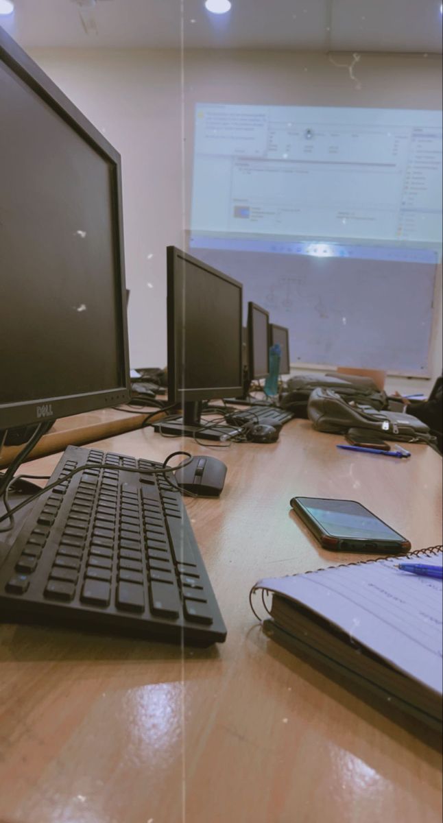 there are many computers on the desk with notebooks and papers in front of them